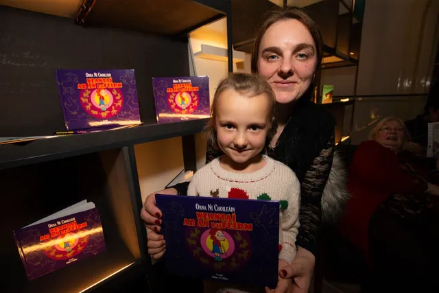 Orna Ní Choileáin agus léitheoir óg ag seoladh an leabhair Neansaí ar an bhFeirm, cóip den leabhar ina lámha acu.
